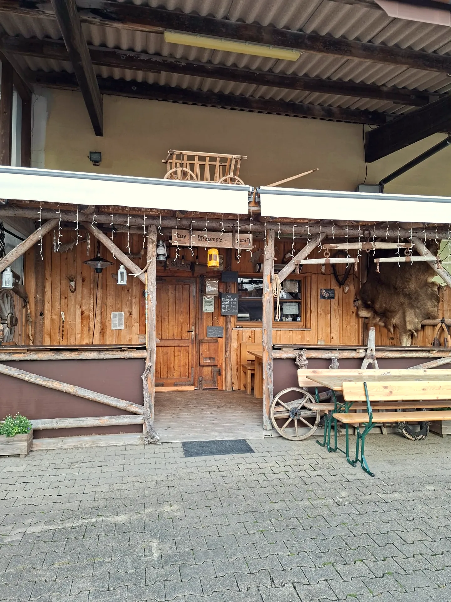 Außenansicht des Saloons zur Maurerzunft mit Holzfassade, Wagenrad und Biertischgarnitur